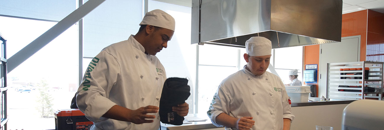 Two male students in chef outfits in a kitchen